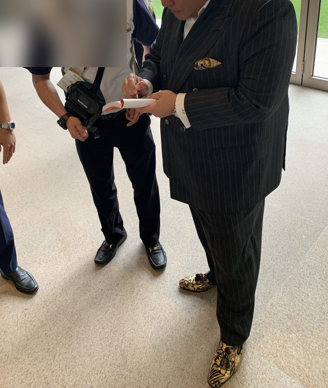 Marcus Lim in tailored pinstripe and gold loafers, signing